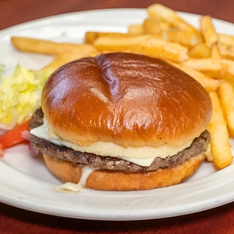 Cheeseburger with melted cheese, lettuce, tomato, and a side of golden french fries on a white plate.