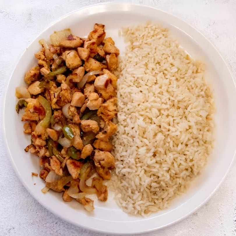 A white plate with fried chicken pieces, green peppers, and onions next to a serving of rice.