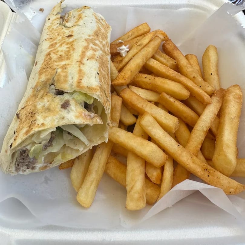 A chicken wrap with shredded lettuce and a side of golden french fries in a white takeout container.