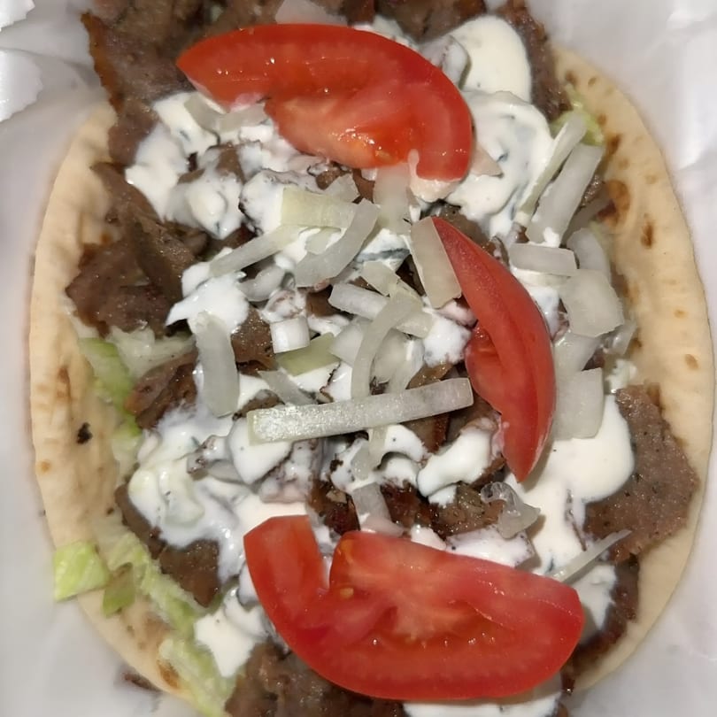 Gyro with sliced meat, lettuce, onions, tomatoes, and white sauce on pita bread.