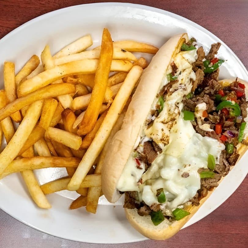 A cheesesteak sandwich with melted cheese, peppers, and onions, served with a side of golden fries.